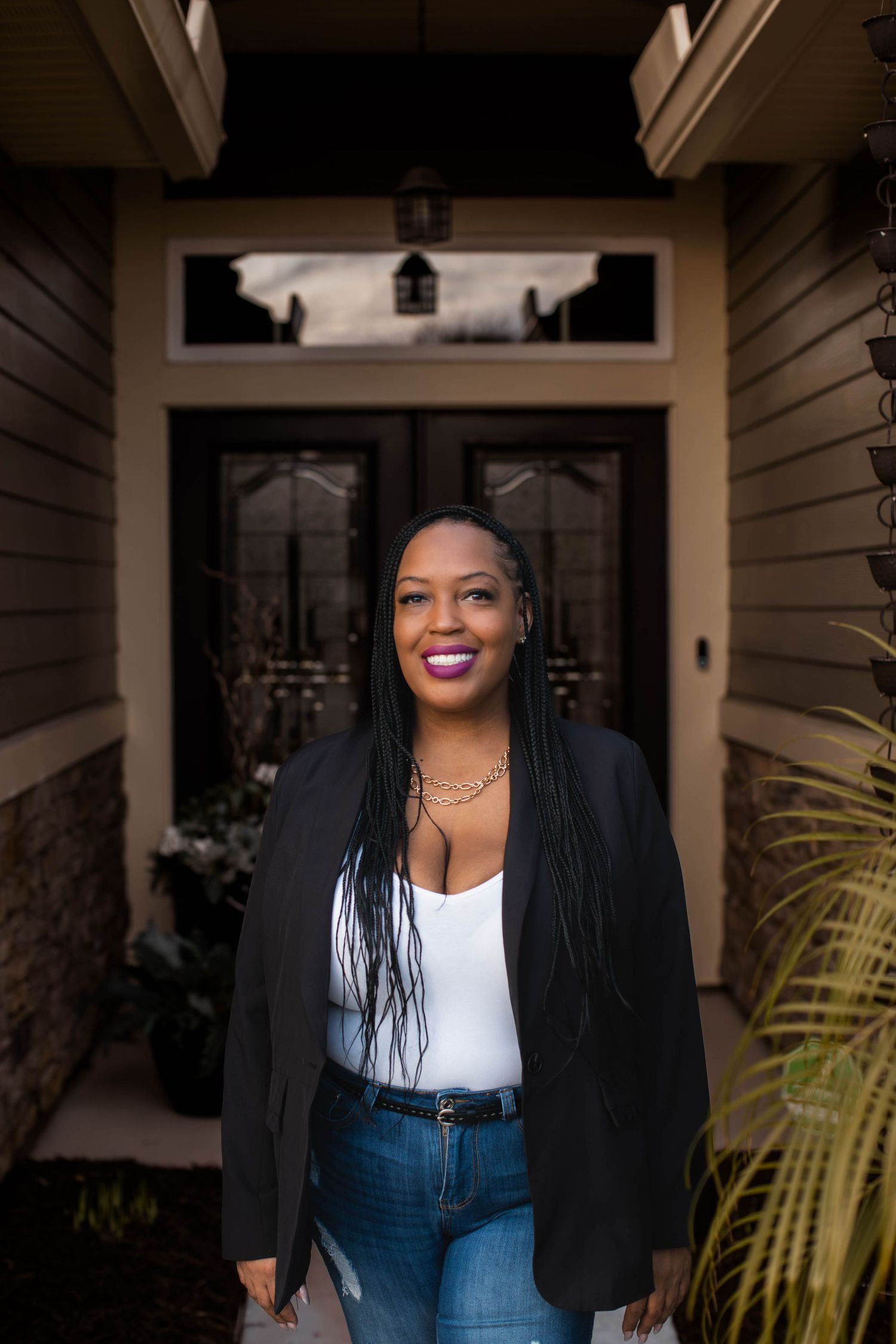Portrait of woman in casual attire standing in front of modern house entrance.