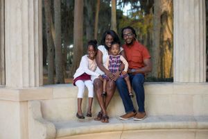 Happy Black family of four smiling together at outdoor stone monument.
