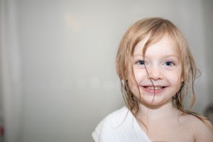 Smiling young child with wet blonde hair wrapped in white towel after bath, portrait photo.