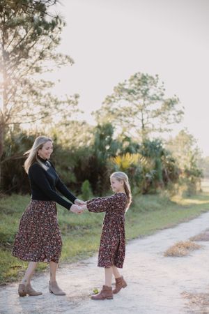 Mother and daughter holding hands in matching floral dresses on a sunlit path.
