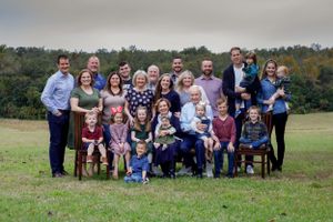 Large multigenerational family portrait outdoors on green grass with trees in background.
