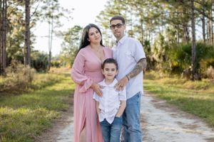 Family of three posing on a wooded path during outdoor portrait session.