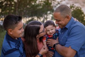 Loving family of four laughing together outdoors at sunset with baby.
