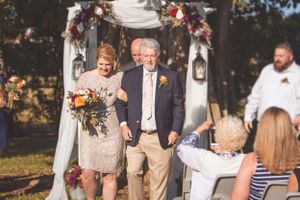 Couple walking down wedding aisle under floral arch at outdoor ceremony.