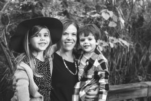 Black and white portrait of smiling mother with two children outdoors.