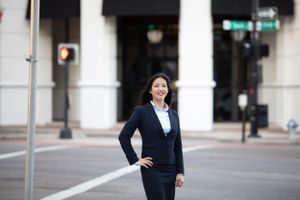 Professional woman in navy business suit posing confidently on urban city street.