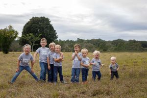 Group of seven young blonde boys posing together in an open grassy field.