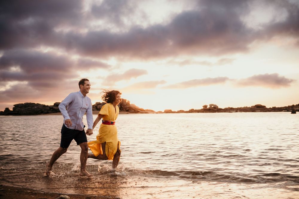 Joyful couple splashes in ocean water during sunset photoshoot on beach.