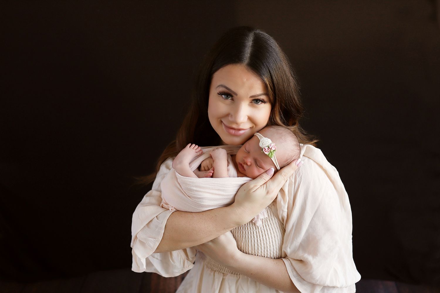 Sweet portrait showing tender embrace with sleeping newborn against dark background.