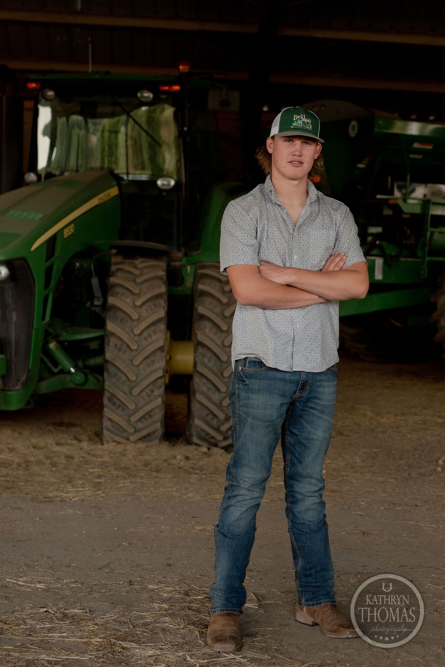 Farmer stands confidently in front of a green John Deere tractor inside a barn.