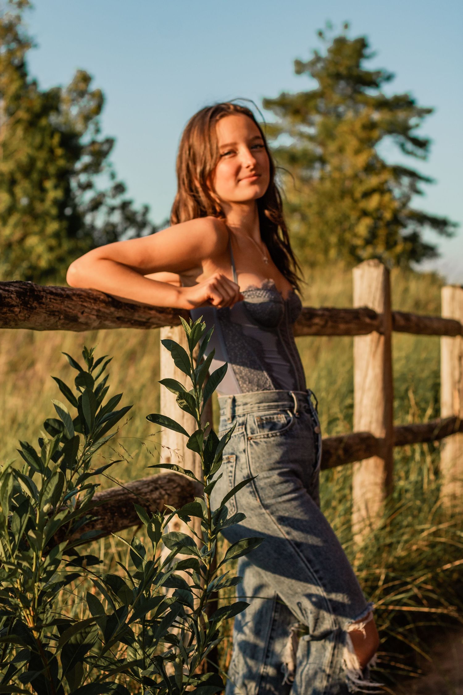 Summer outdoor portrait with rustic wooden fence and greenery in warm evening light.