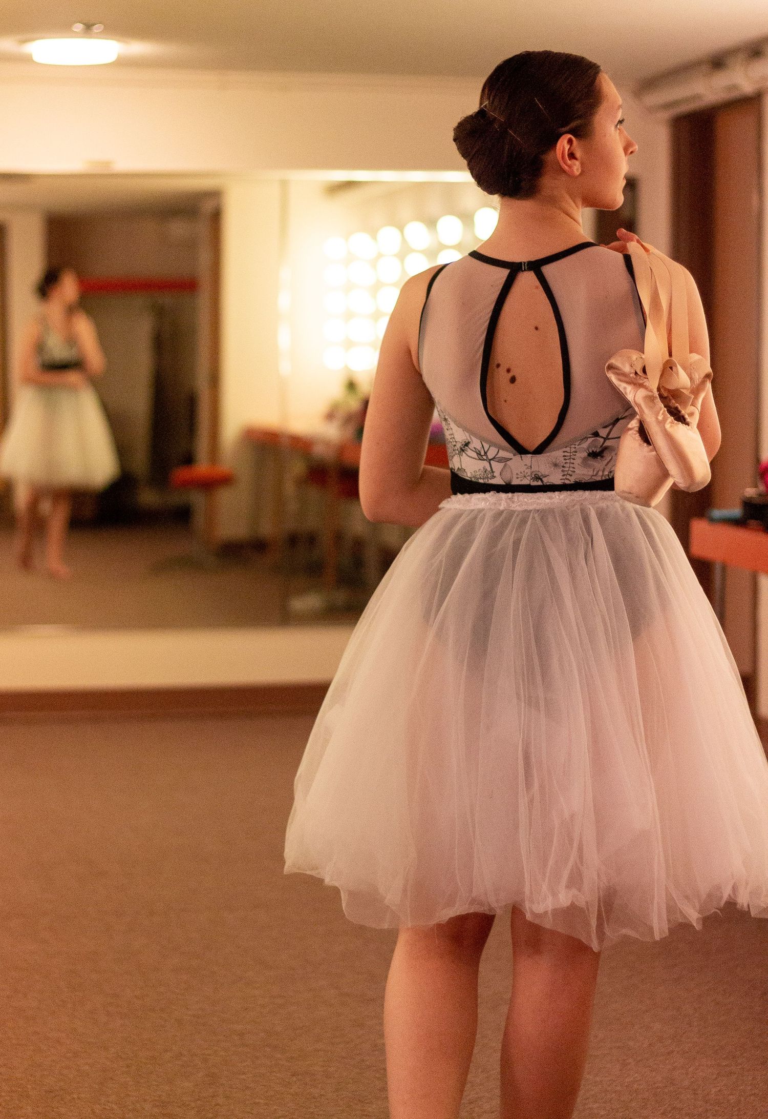 A dancer in a tulle dress poses elegantly in front of a mirror in a ballet studio.