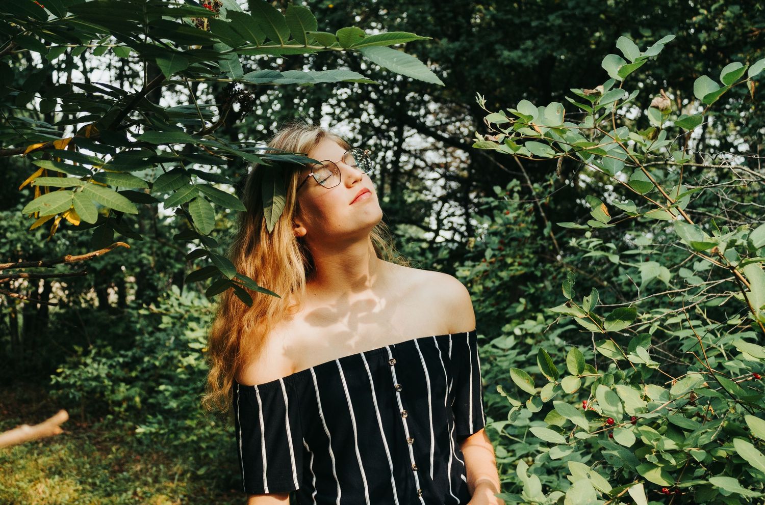 A dreamy portrait in dappled sunlight through trees of someone wearing a striped off-shoulder top.