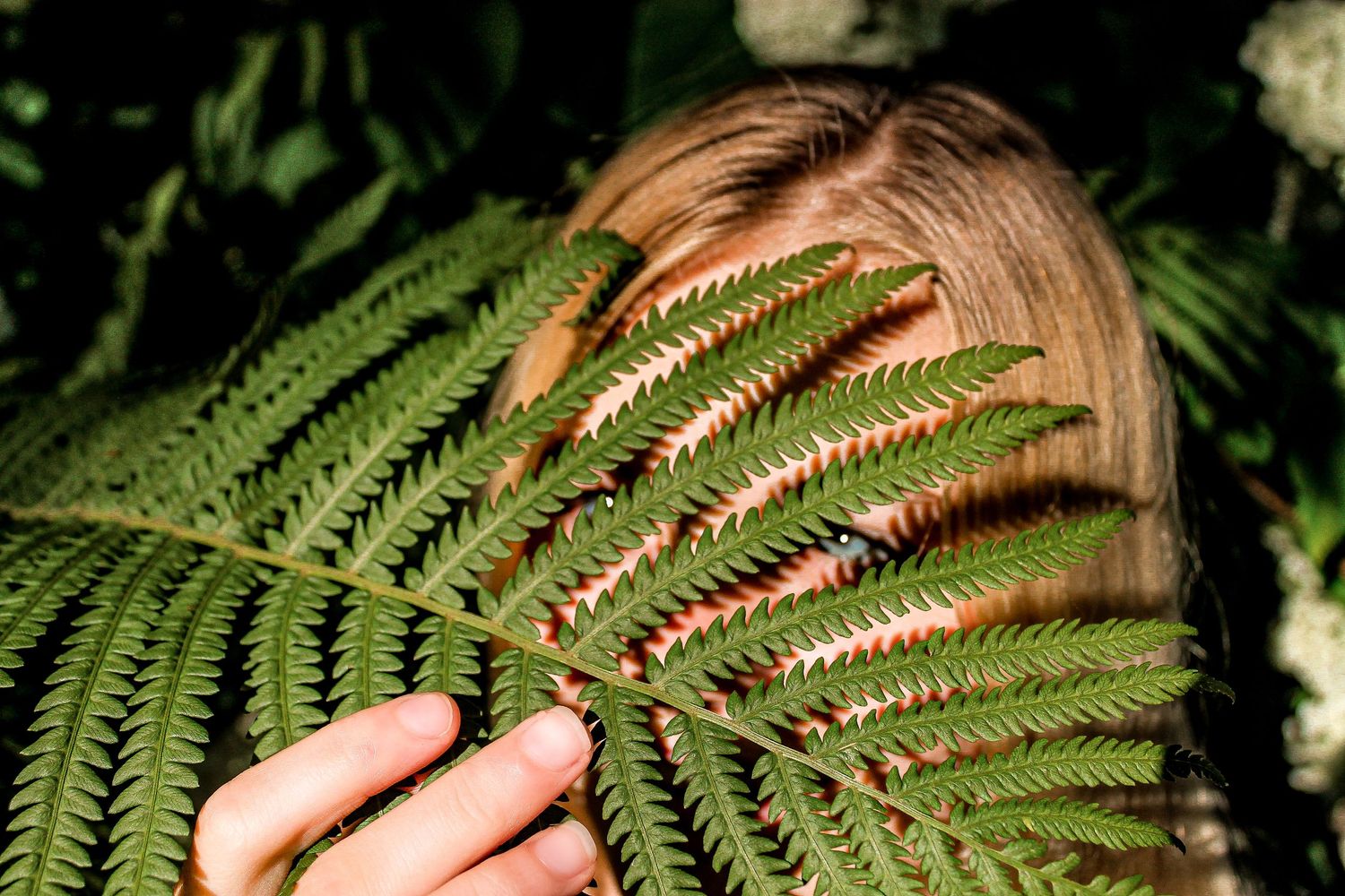 Creative portrait partially obscured by a fern frond in natural lighting.