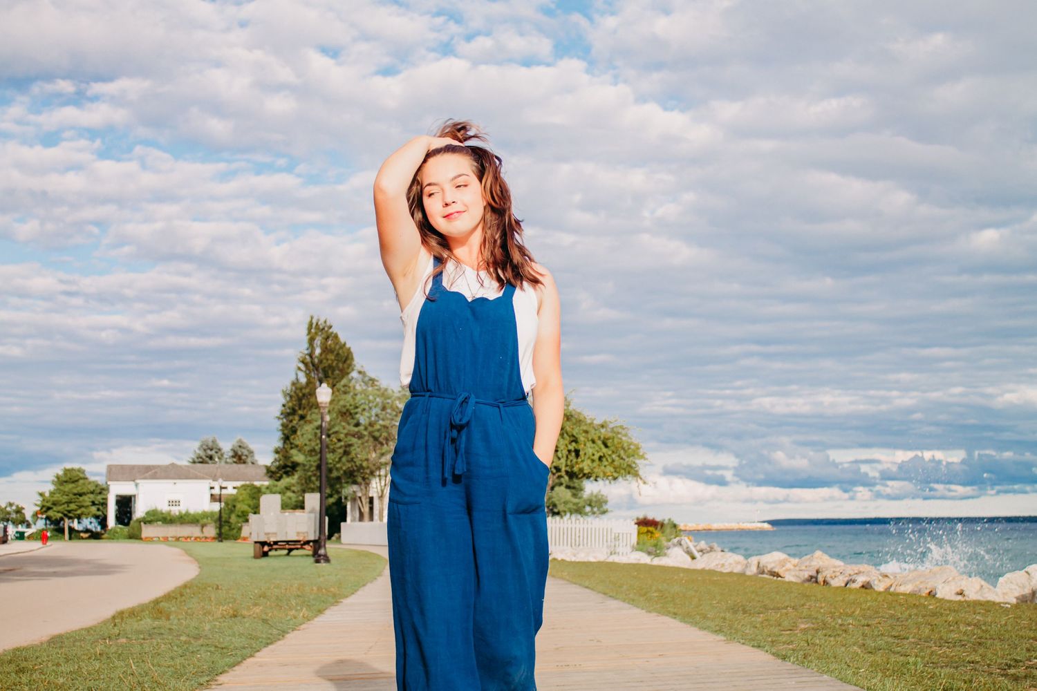 A blue maxi dress flows in the breeze against a scenic waterfront backdrop with cloudy skies.