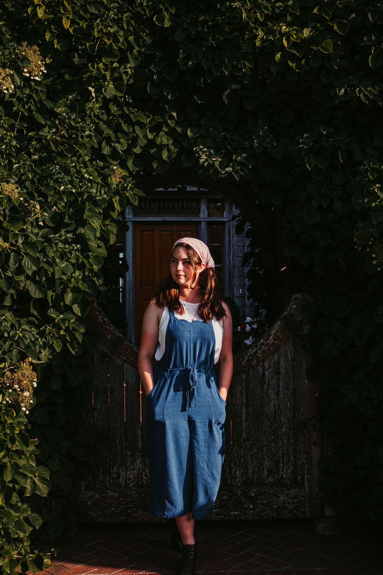 Denim overalls stand out against lush garden foliage and a rustic wooden door.
