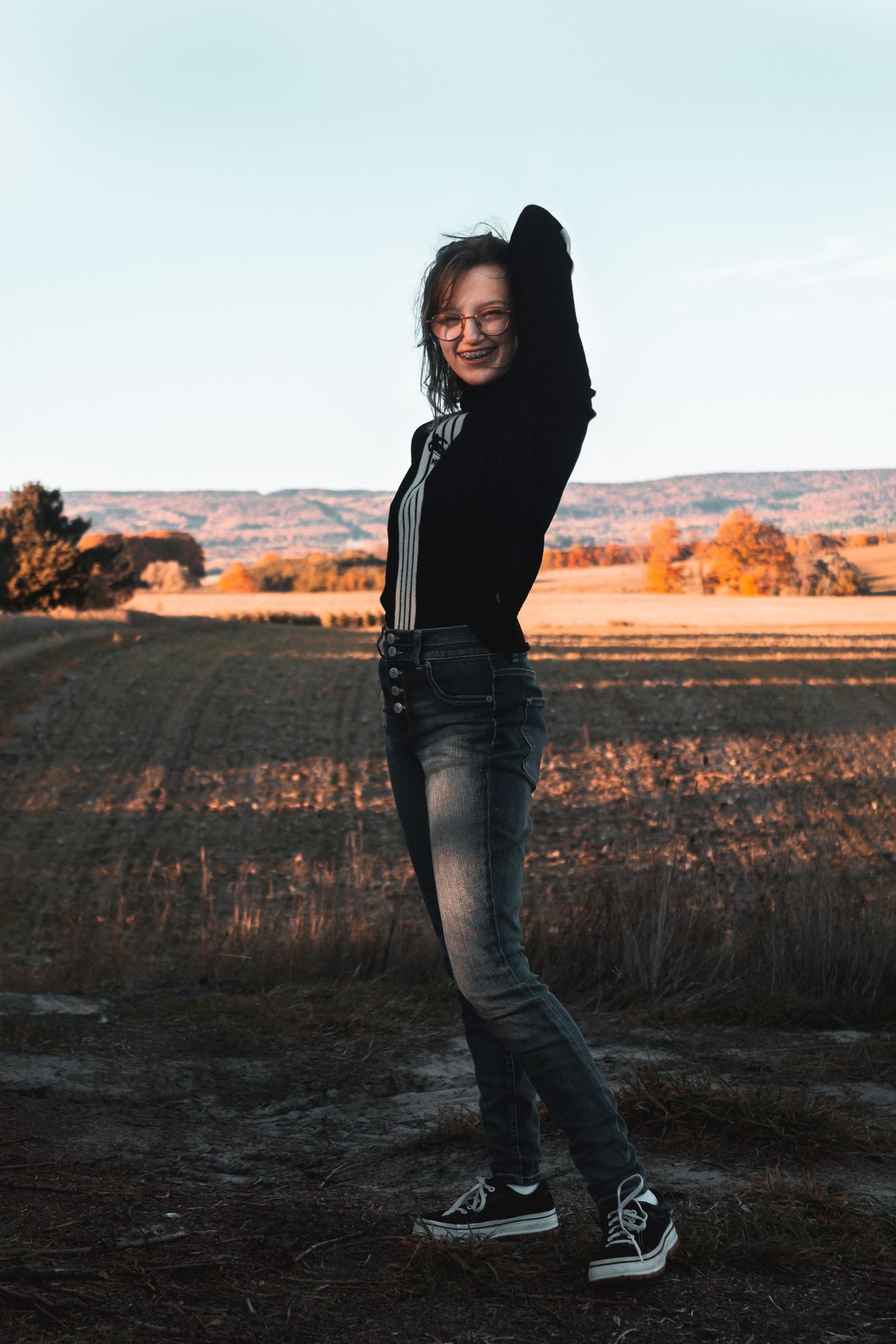 Silhouette against autumn landscape wearing black jacket and jeans in golden sunset light.