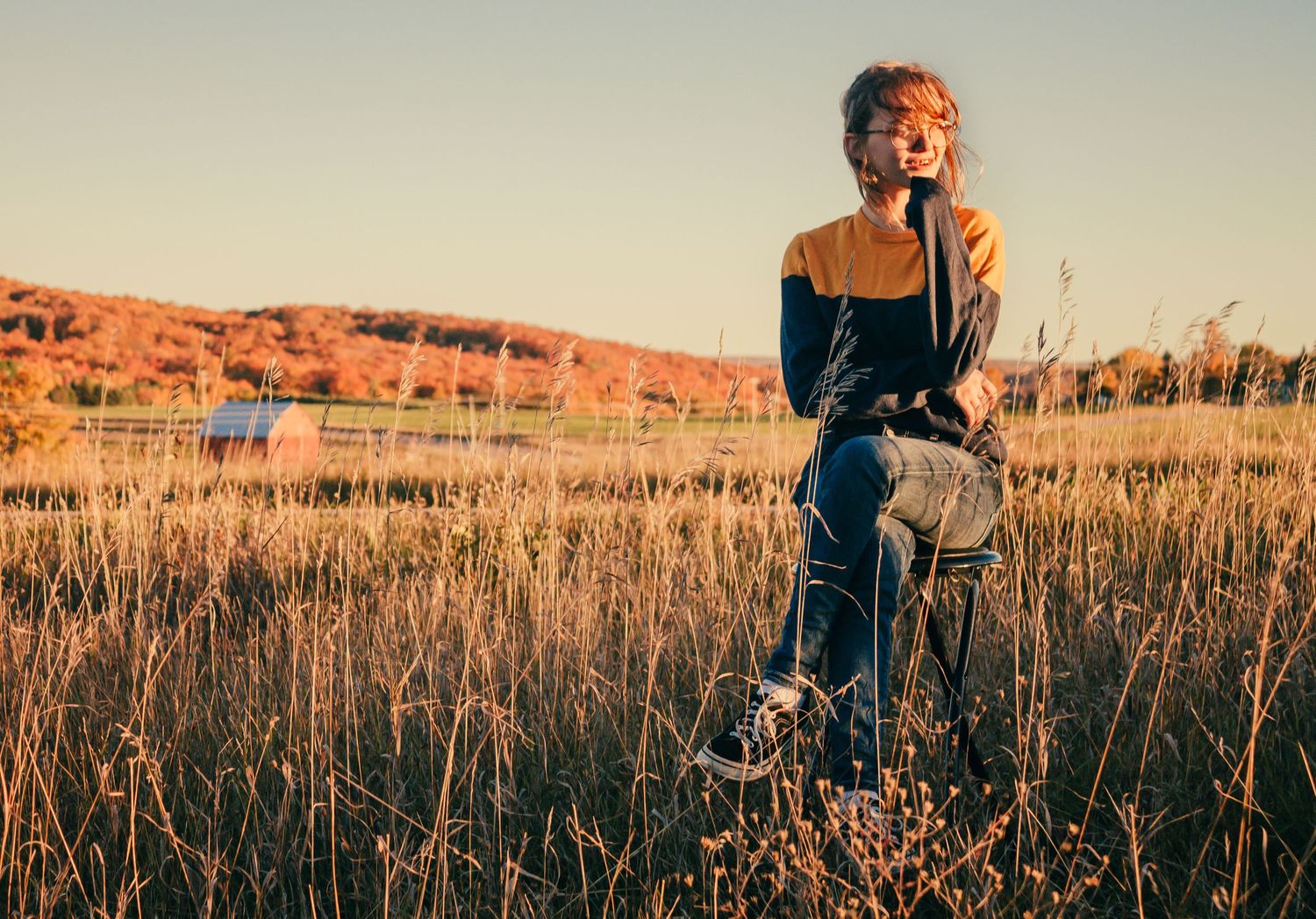Portrait in tall grass field during golden hour with mountains in background.