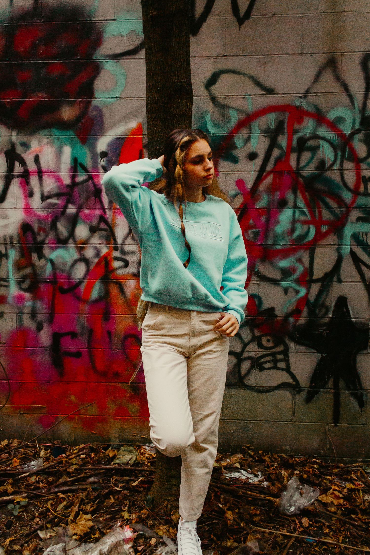 Fashion portrait against colorful graffiti wall featuring mint sweater and white pants outfit.