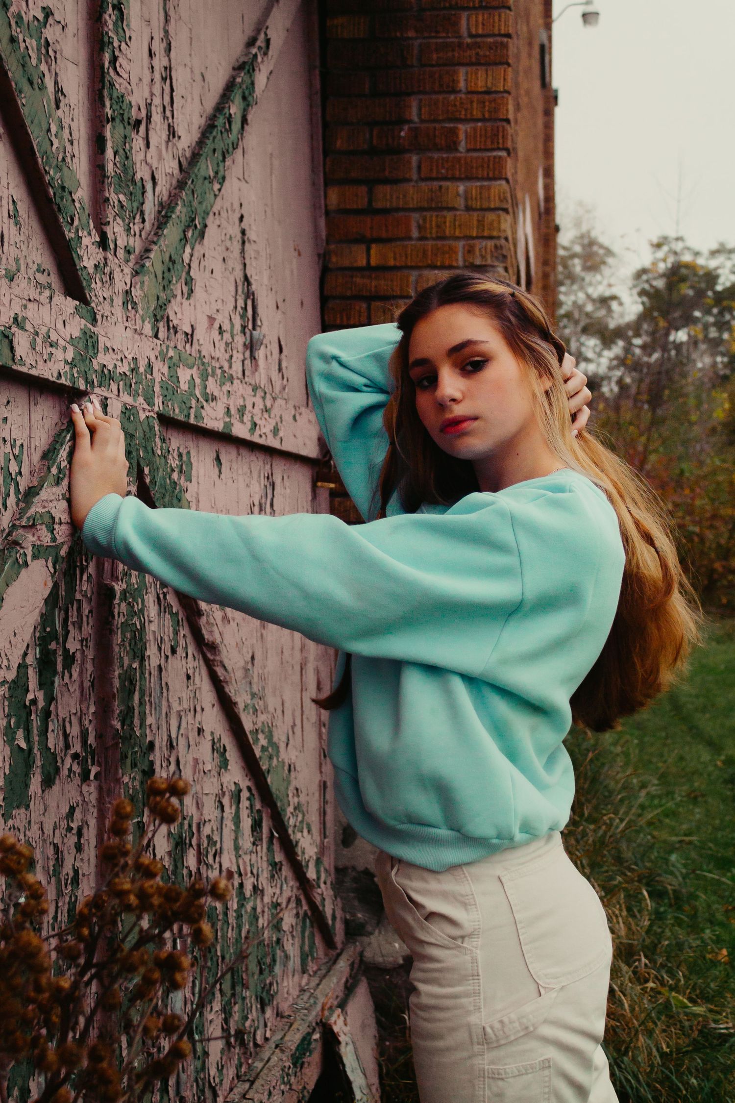 Fashion model in mint green sweater poses against weathered pink wall with vintage architectural details.