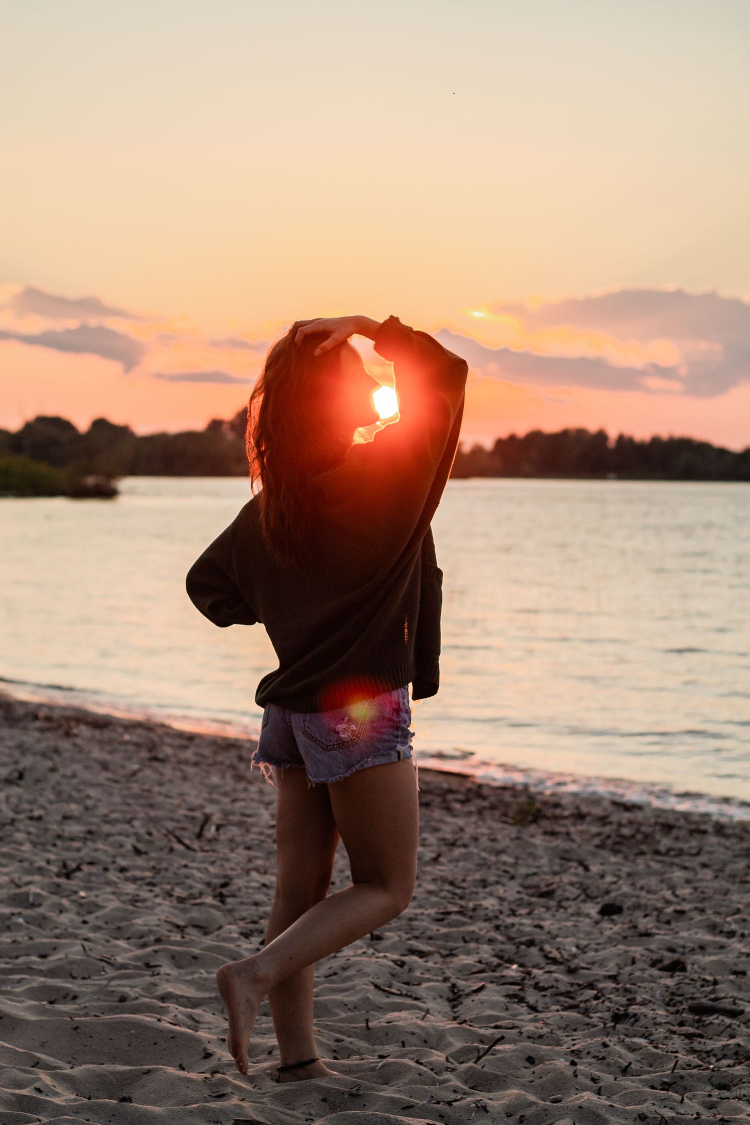 Silhouette on beach at sunset with orange sky and water backdrop.