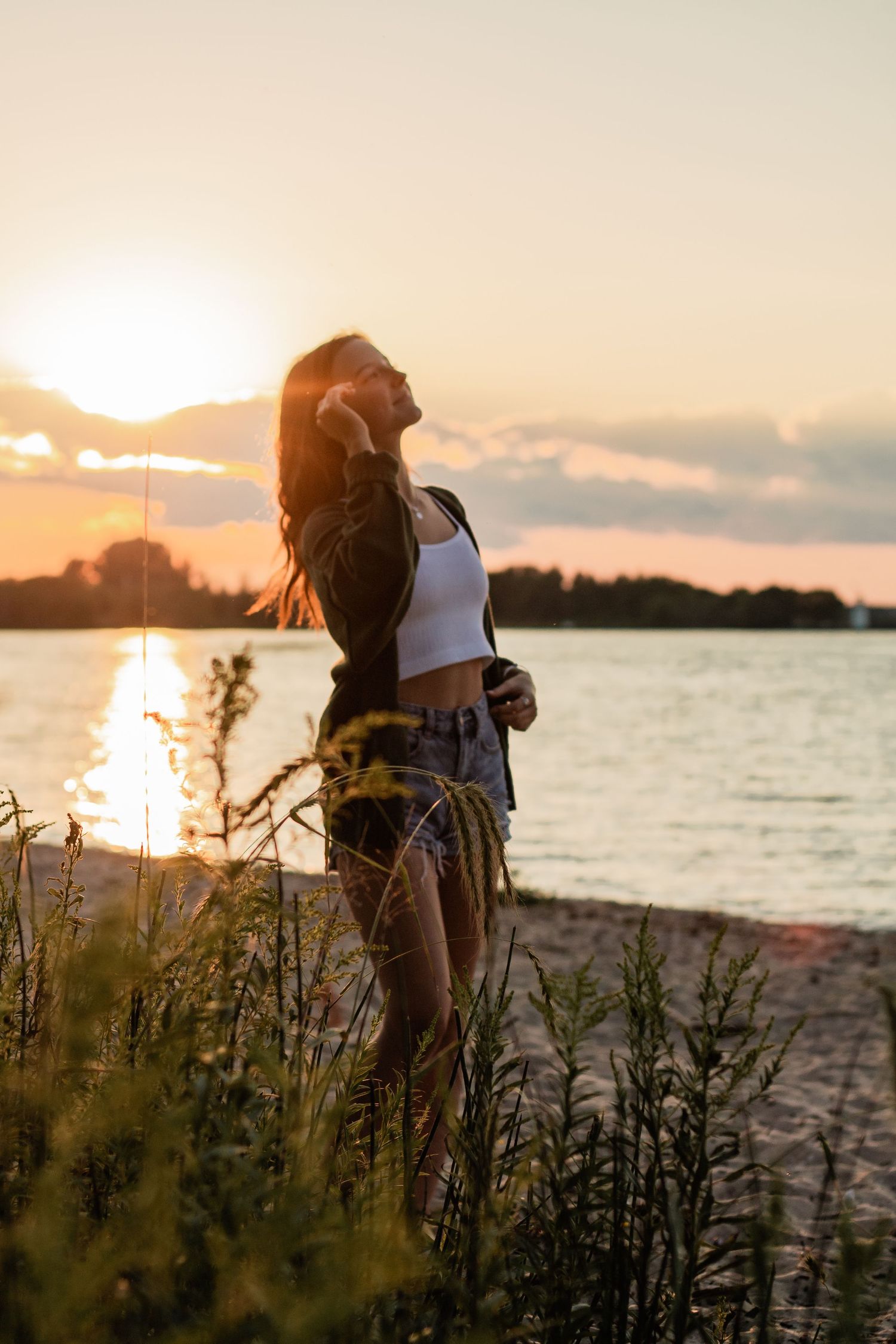 Sunset beach silhouette with golden light reflecting off water and wild grasses.