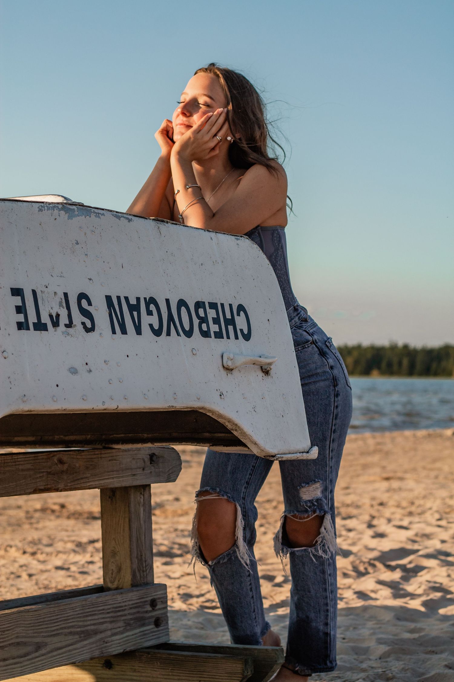 Relaxed beach pose against white lifeguard station with lake and trees in background.