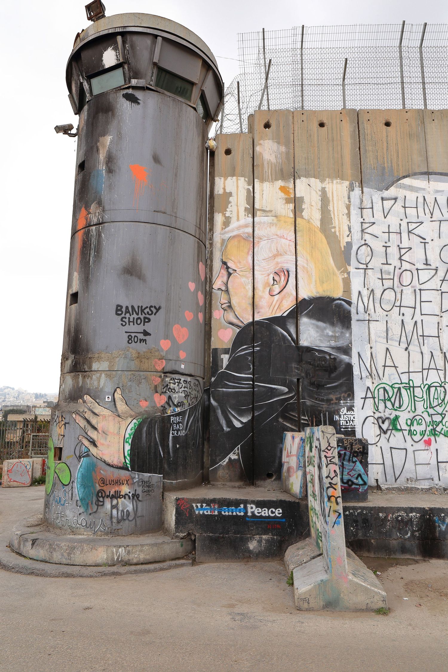 Graffiti art on a security tower and concrete barrier wall featuring street art by Banksy.