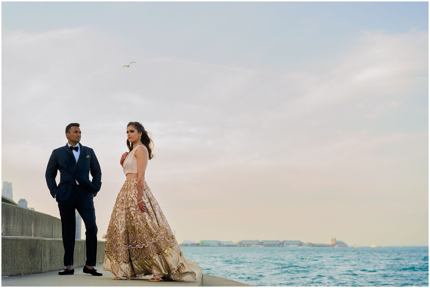 Elegant couple in formal attire posing by the waterfront during sunset.