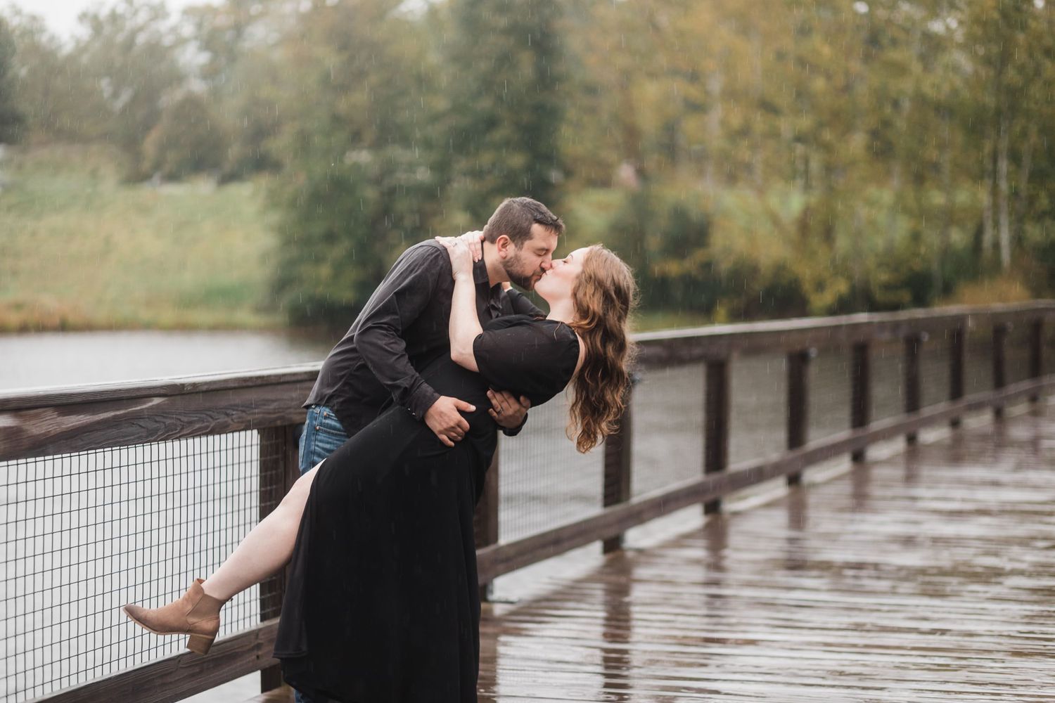 Couple sitting close together on wooden walkway by tranquil lake on cloudy autumn day.