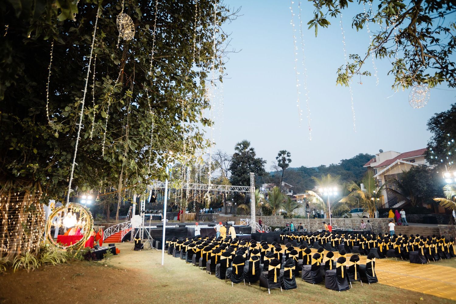 Rows of guests seated at an outdoor evening ceremony with glowing decor and trees in the background.
