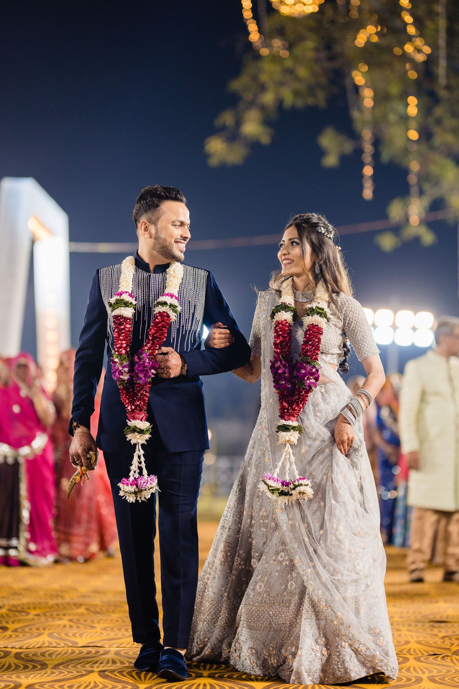 Couple walking together at night wearing traditional wedding attire with floral garlands.