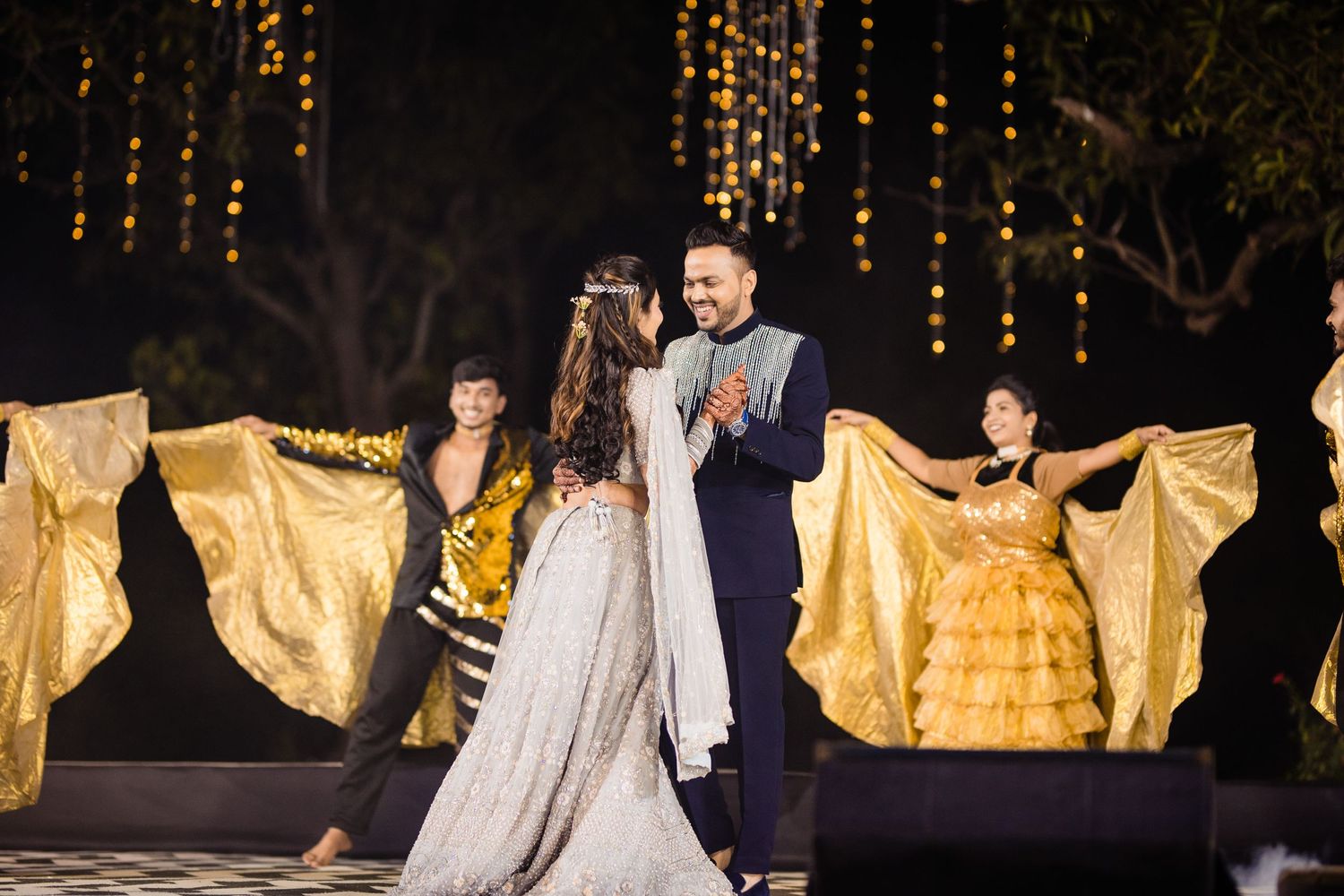 Performers in flowing gold and white costumes dance dramatically on a dimly lit stage.