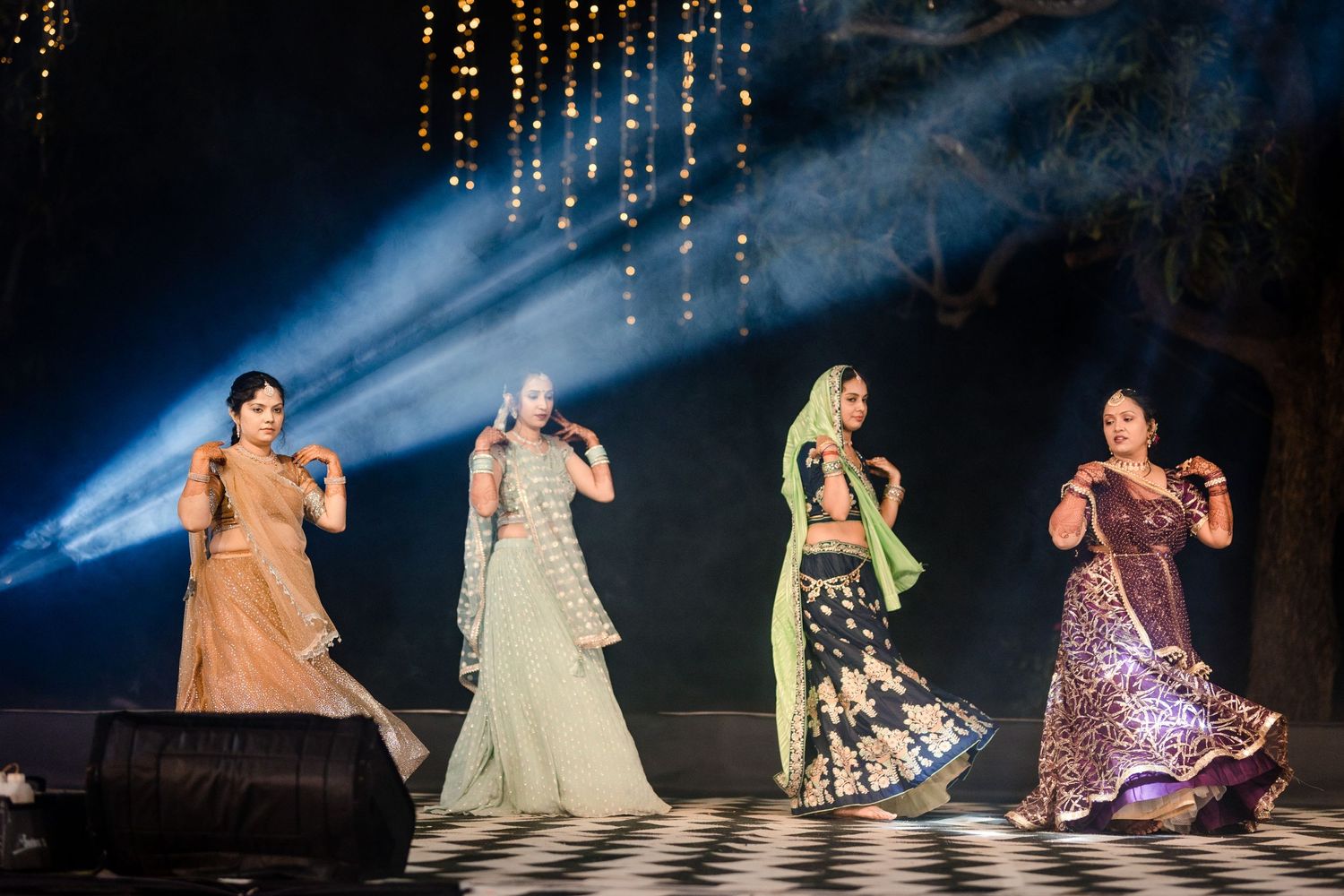 Group dance performance featuring elegant traditional costumes under hanging string lights.