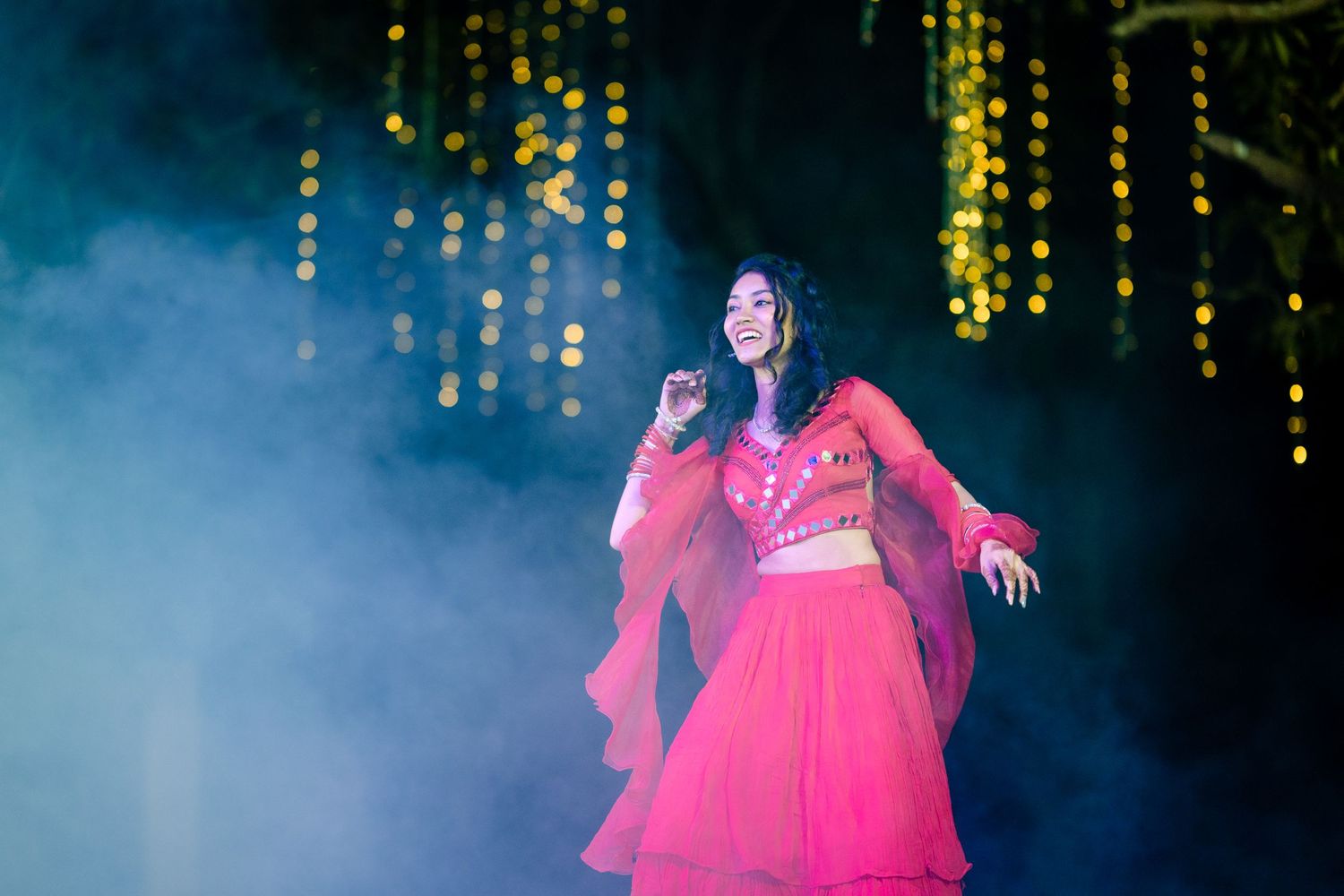 Dramatic stage performance with dancers in vibrant pink costumes against blue lighting.