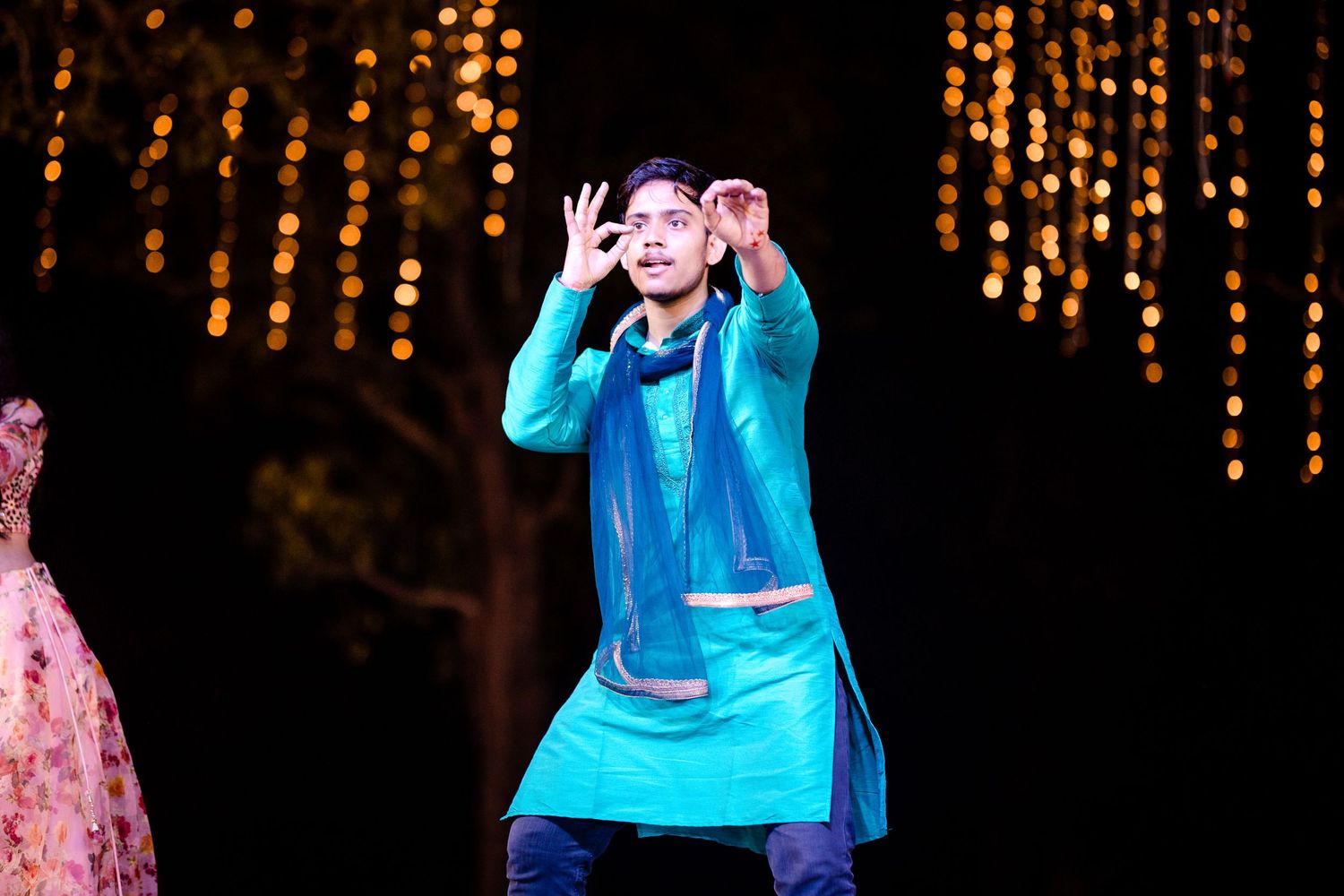 Performers in bright turquoise and pink costumes dance energetically on stage.