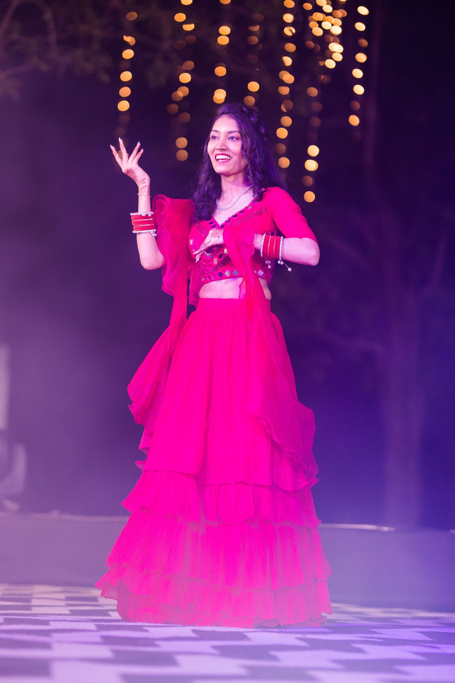 A performer in a vibrant red ballgown dances gracefully on a misty stage with twinkling lights in the background.