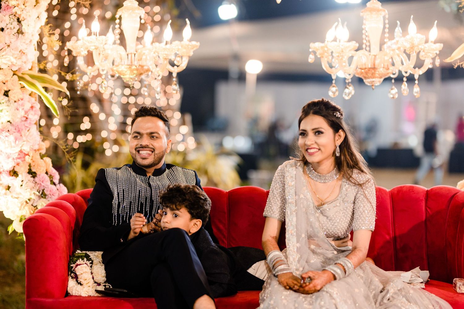 Wedding guests enjoy festivities beneath ornate crystal chandeliers in a luxurious indoor venue.