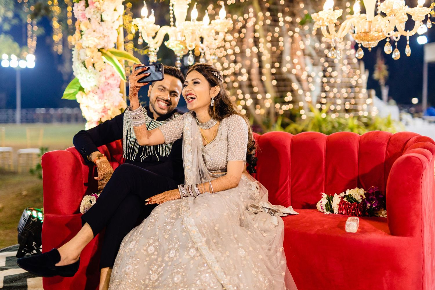 Couple celebrates on a plush red couch under sparkling chandeliers at their reception.