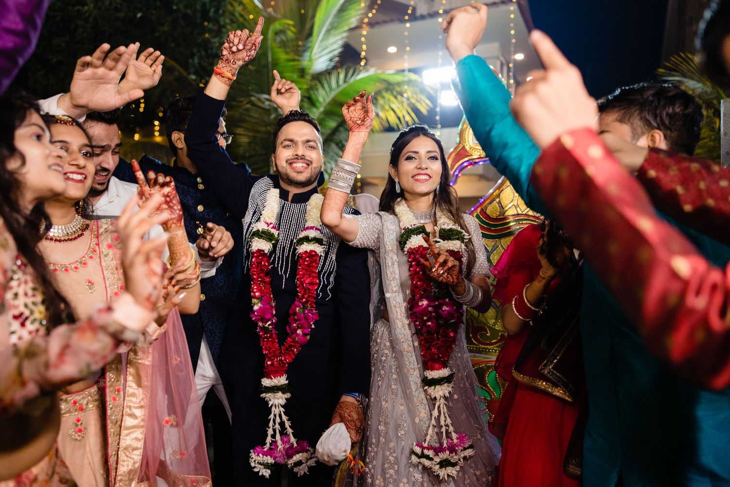 Guests dance and celebrate at a vibrant wedding reception with colorful lighting and decor.
