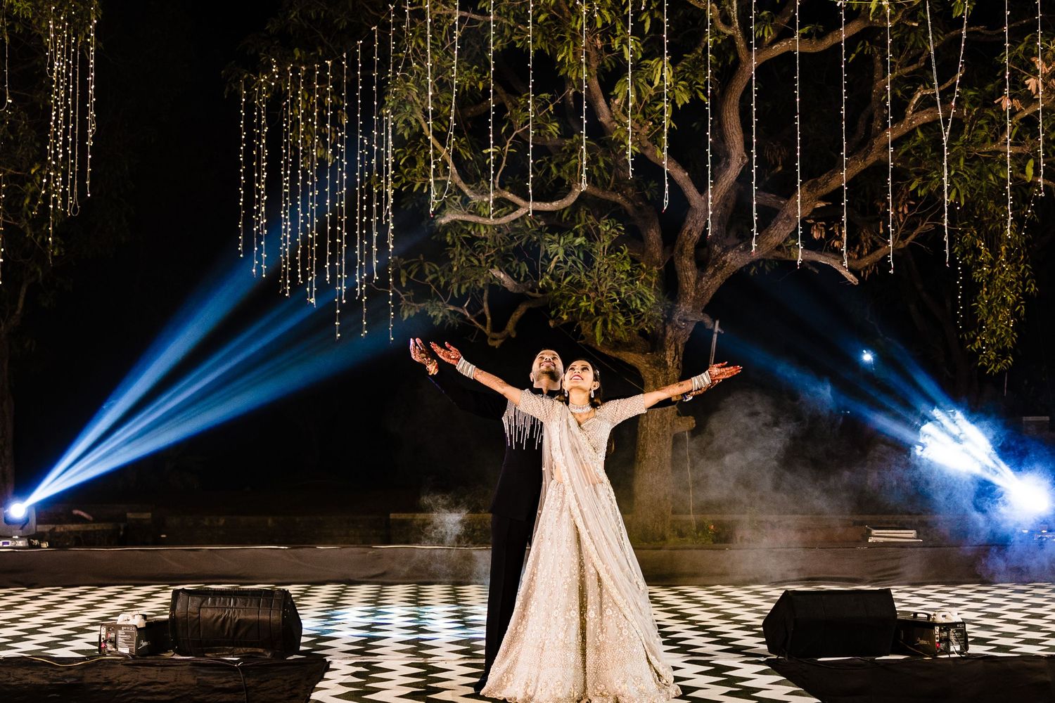 Theatrical performance with dramatic blue spotlights and fog effects on a checkered stage floor.