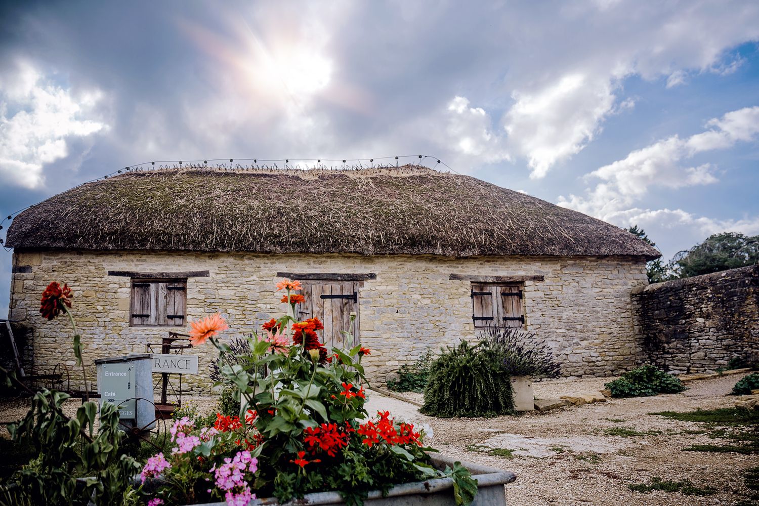 Traditional stone cottage with thatched roof and colorful flower garden in foreground.
