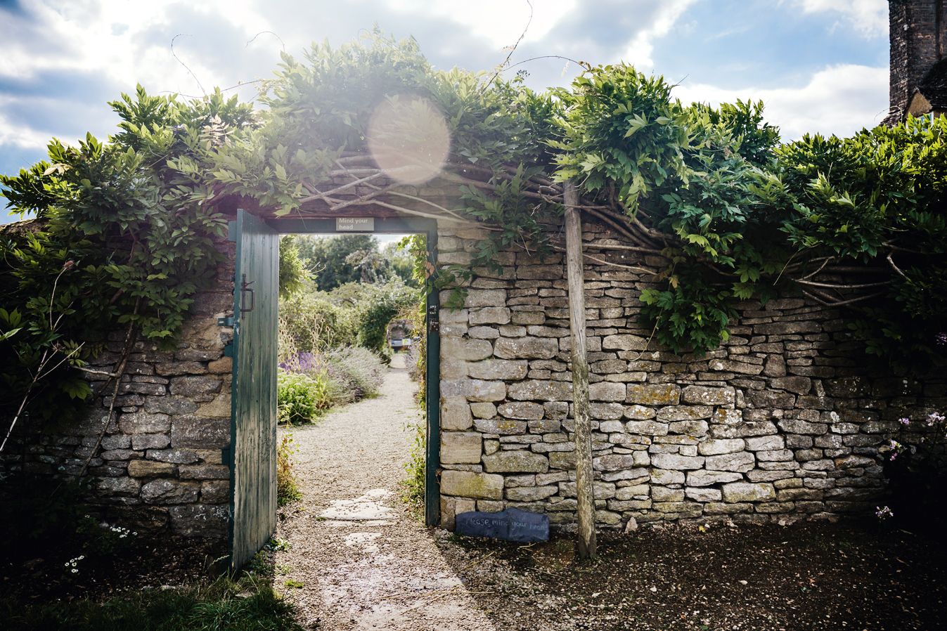 Stone wall archway entrance with sunlit garden path visible through opening.