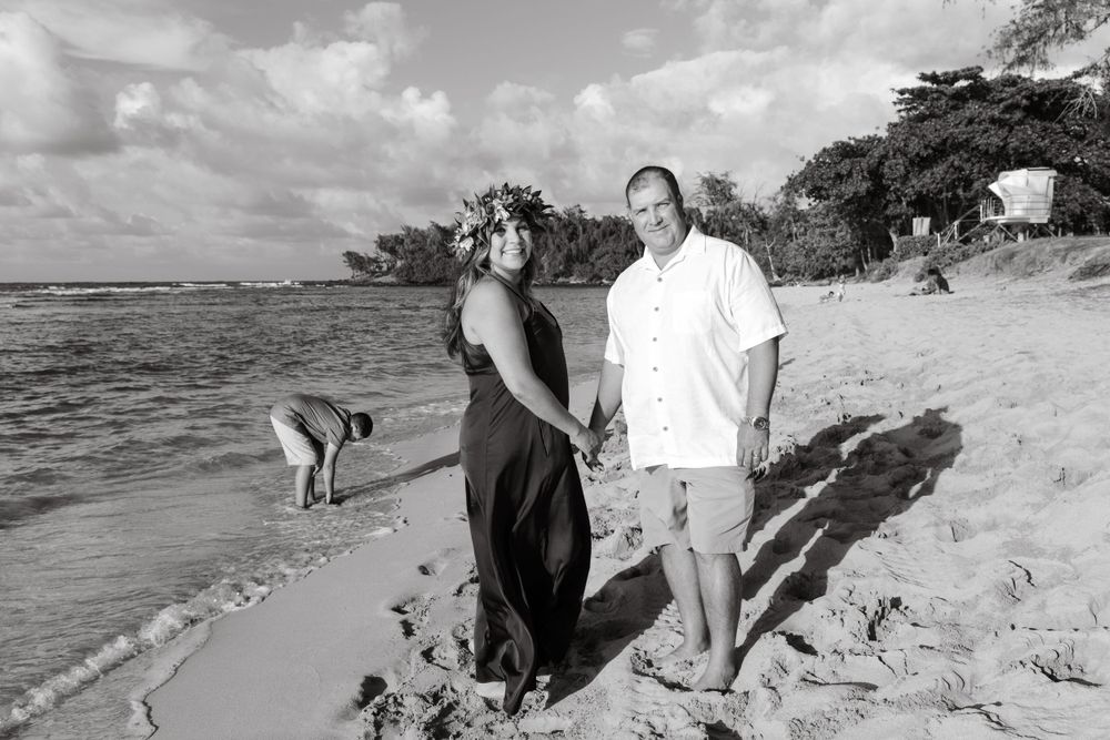 A couple walks along a scenic Hawaiian beach with waves crashing in the background.