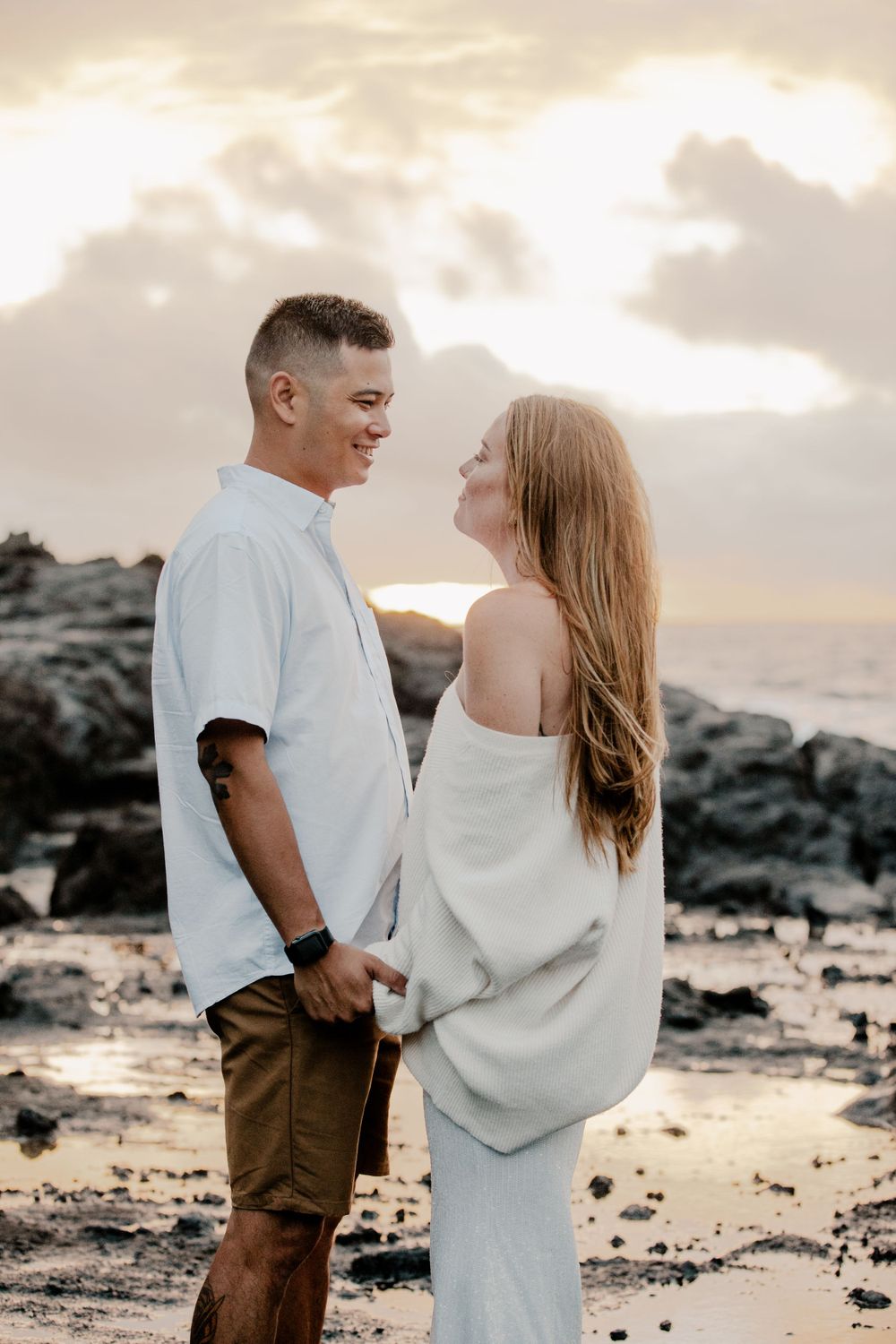 Couple sharing intimate moment on rocky beach at sunset.