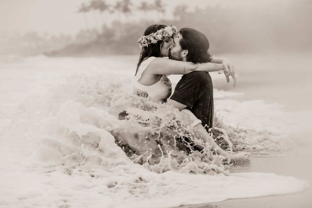 A couple splashes in the ocean waves during a romantic beach photoshoot.