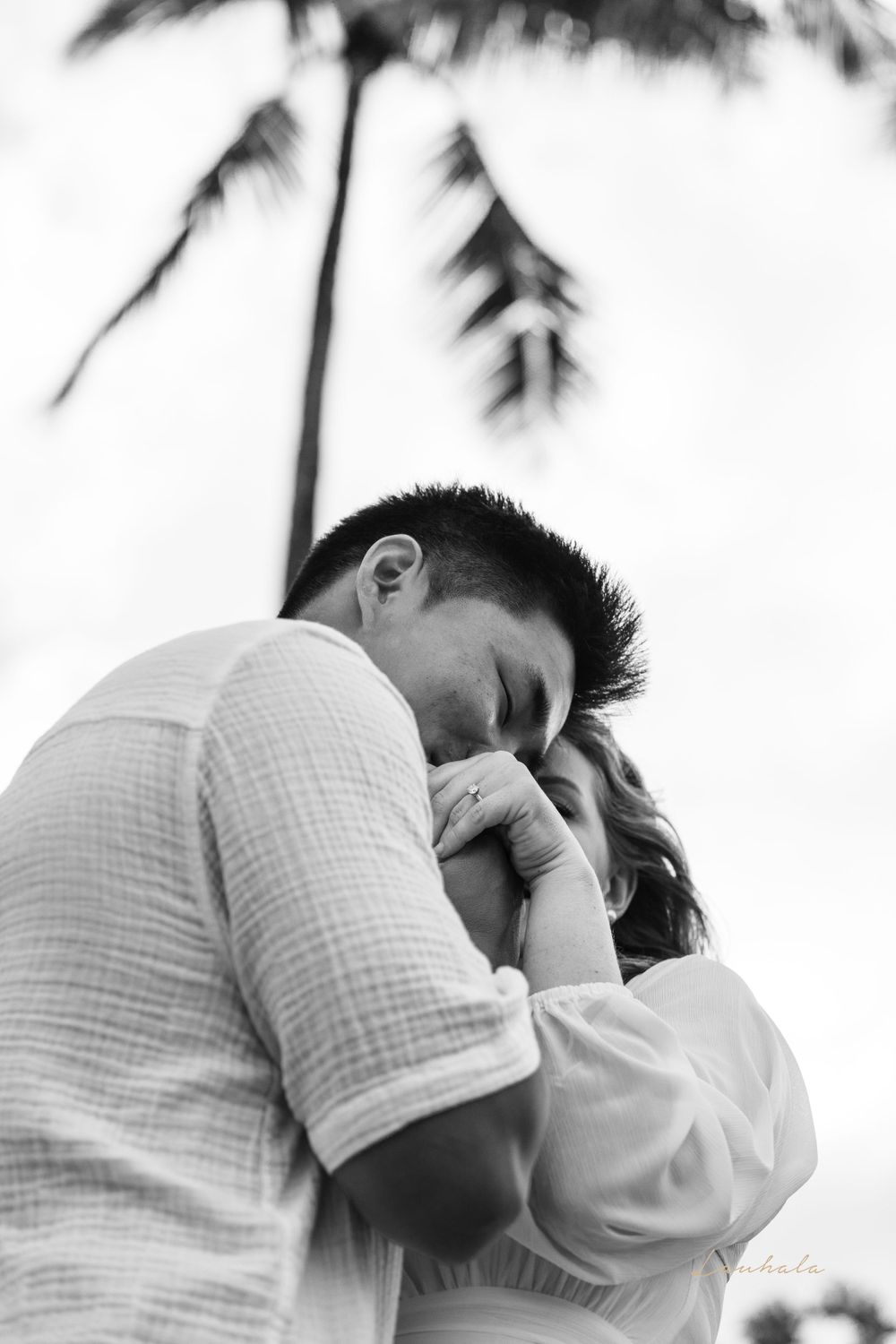 Black and white portrait of couple sharing intimate moment under palm trees.