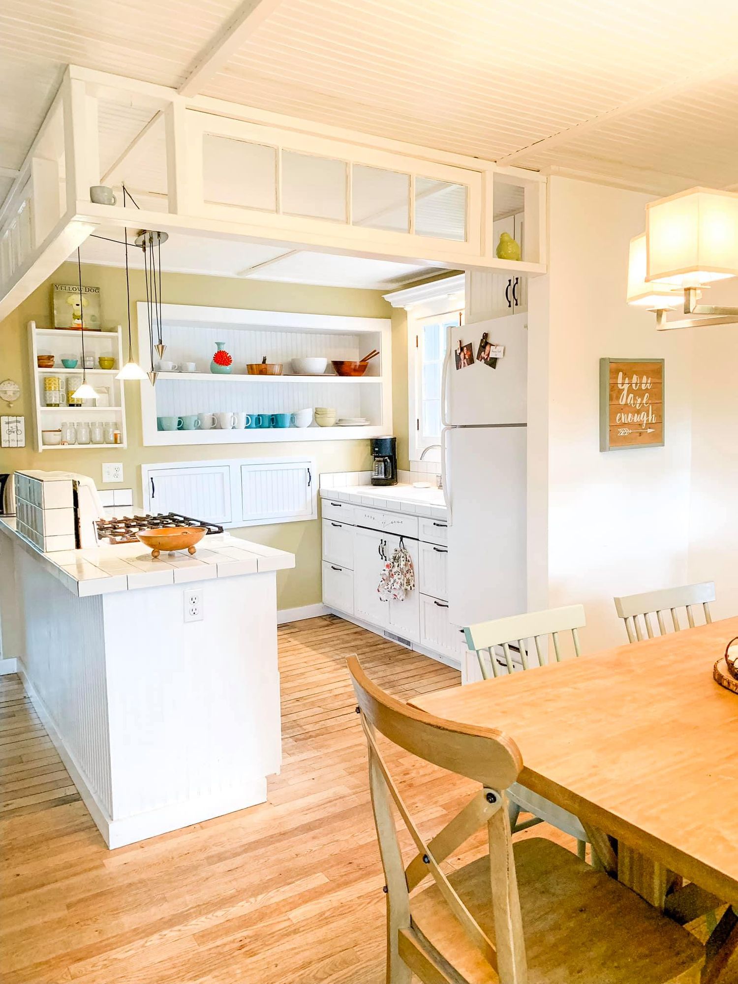 Modern white kitchen with wood floors, open shelving, and a natural wood dining table showcases clean lines and bright design.