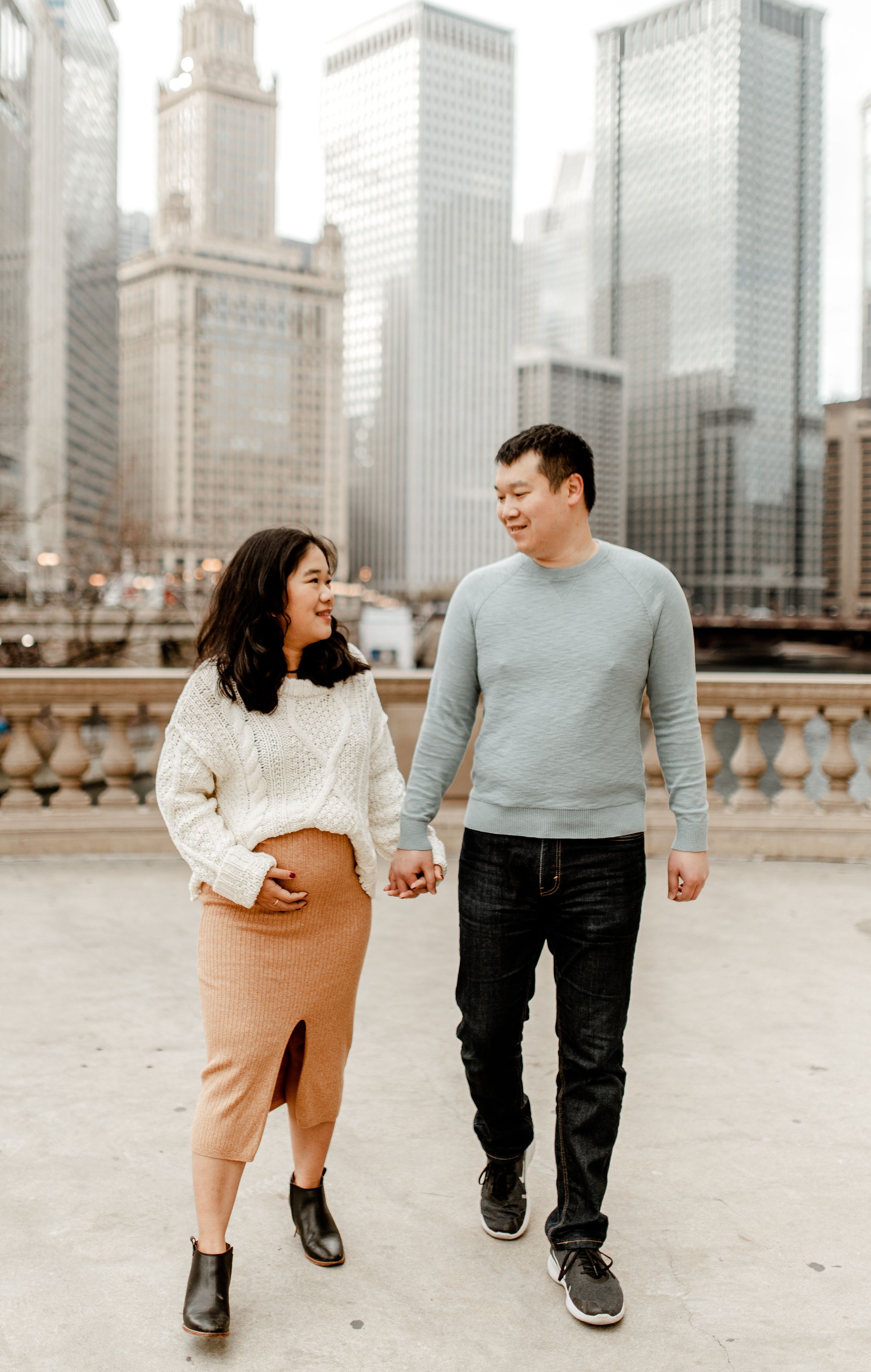A couple walks hand in hand along Chicago's riverfront with iconic skyscrapers in the background.