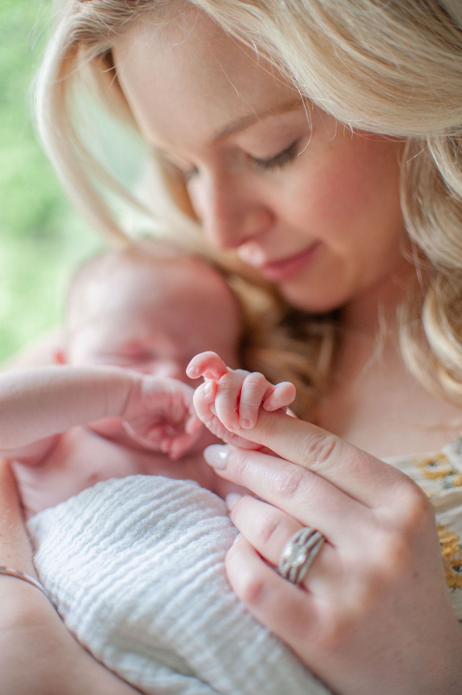 mom holding baby in swaddle and baby is holding moms finger